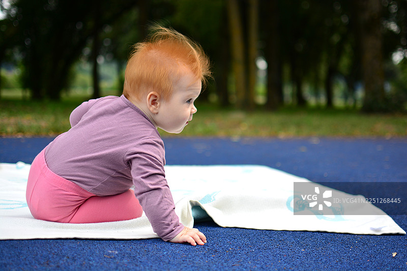 一个可爱的红发宝宝在地垫上爬行，在公园里探索周围的环境图片素材