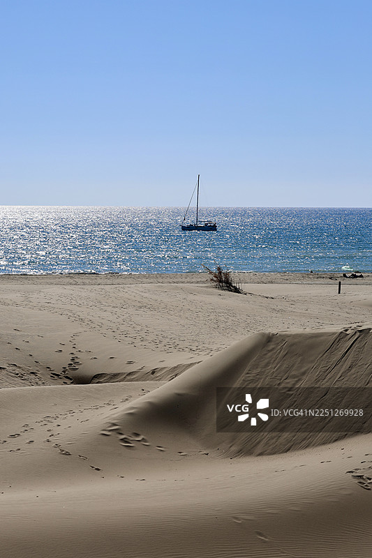 晴朗天空下，波光粼粼的蓝色海洋上有一艘帆船，风景优美的沙滩和沙丘景色图片素材