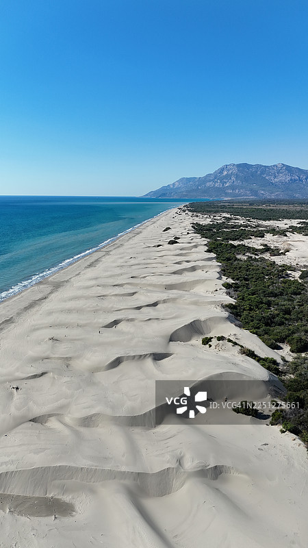 从空中俯瞰，一处原始的海滩，拥有沙丘、碧绿的海洋和远处的山峦，在晴朗的蓝天下图片素材