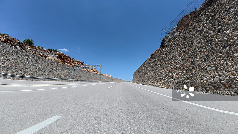 晴朗蓝天下，穿过山口的空旷沥青路，两侧有落石防护墙图片素材