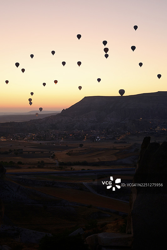 热气球在日落时分的天空中飞翔，掠过风景优美的景色，呈现出令人惊叹的冒险和旅行景象图片素材