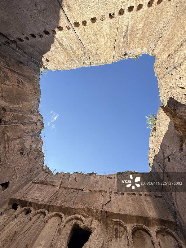 仰视视角拍摄的古代岩石雕刻遗址，背景是湛蓝的天空，展现了历史建筑和自然光线图片素材