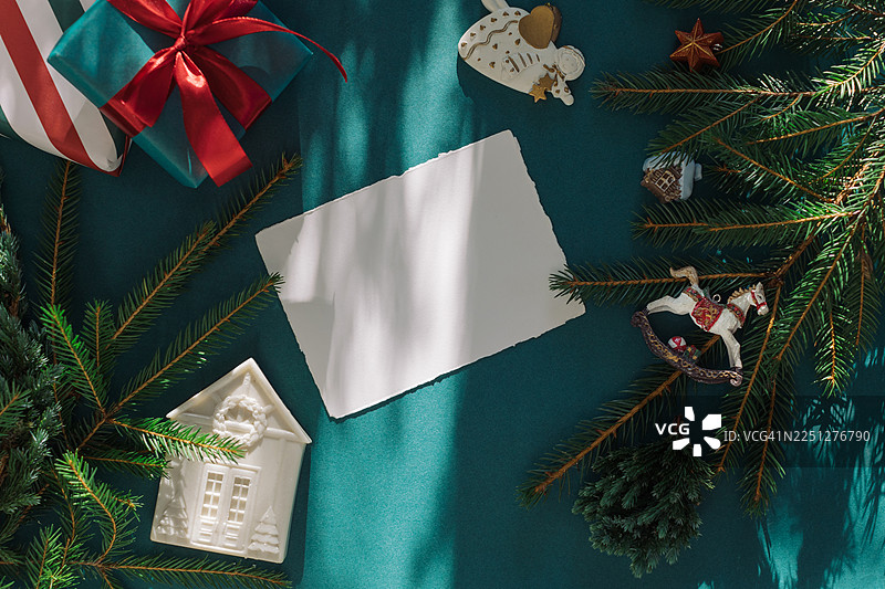 绿色背景上，俯视一张空白的毛边卡片，旁边有包装好的礼品盒、节日圣诞装饰品和松枝图片素材