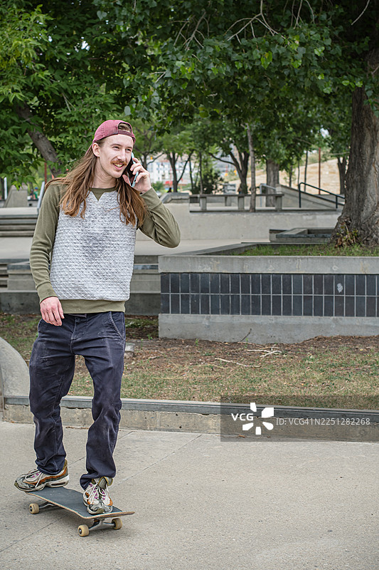 滑板爱好者在户外边玩手机边玩滑板图片素材