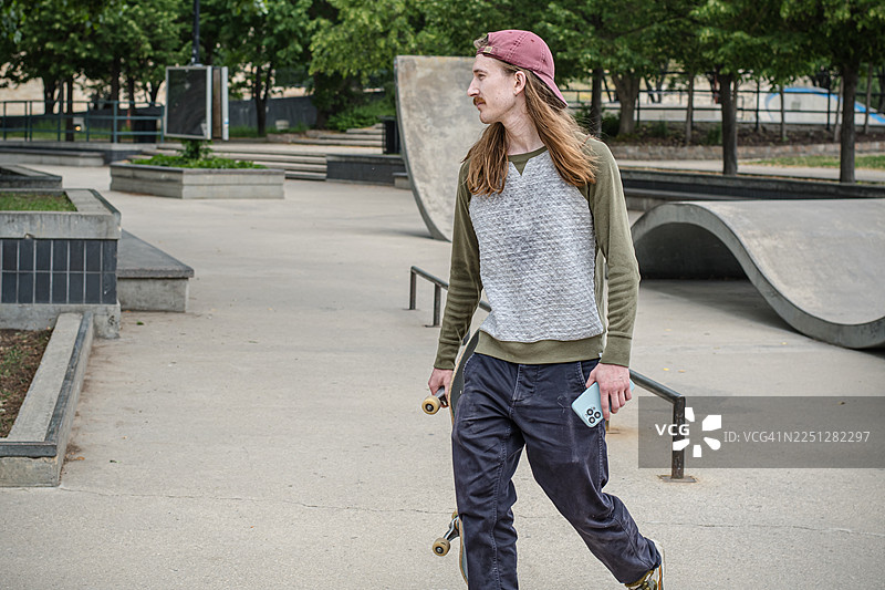 年轻的滑板爱好者在户外使用手机图片素材