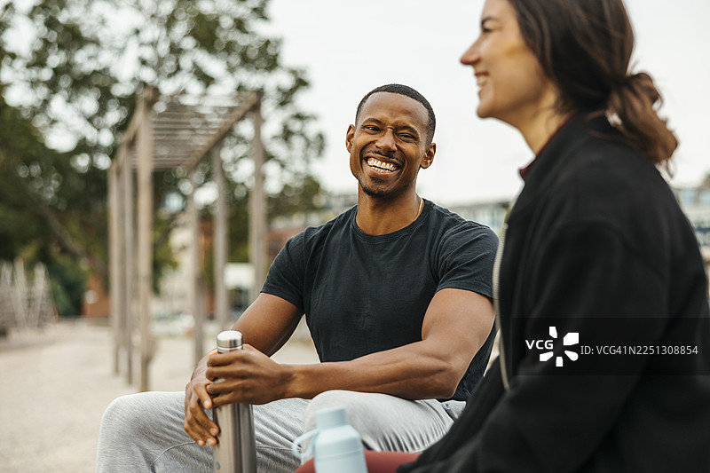 快乐的男人坐在公园的健身房里，和女朋友一起拿着水瓶图片素材