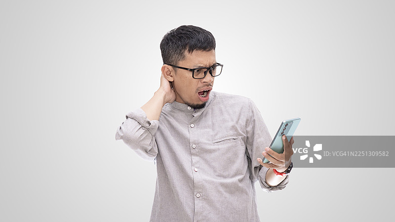 亚洲男子震惊地看着智能手机，露出惊恐的表情图片素材