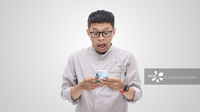 亚洲男性震惊地看着智能手机的惊恐表情图片素材