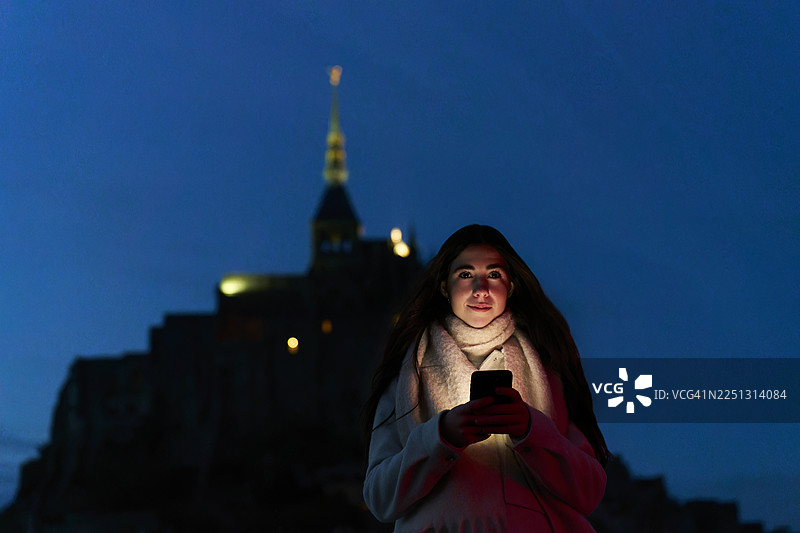 女子夜晚使用手机游览圣米歇尔山图片素材
