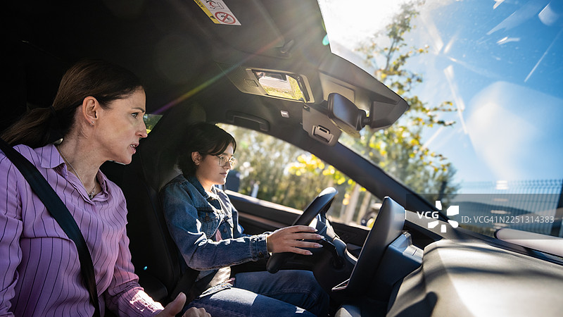 粉色衬衫的驾驶教练观察穿着牛仔夹克的年轻司机图片素材