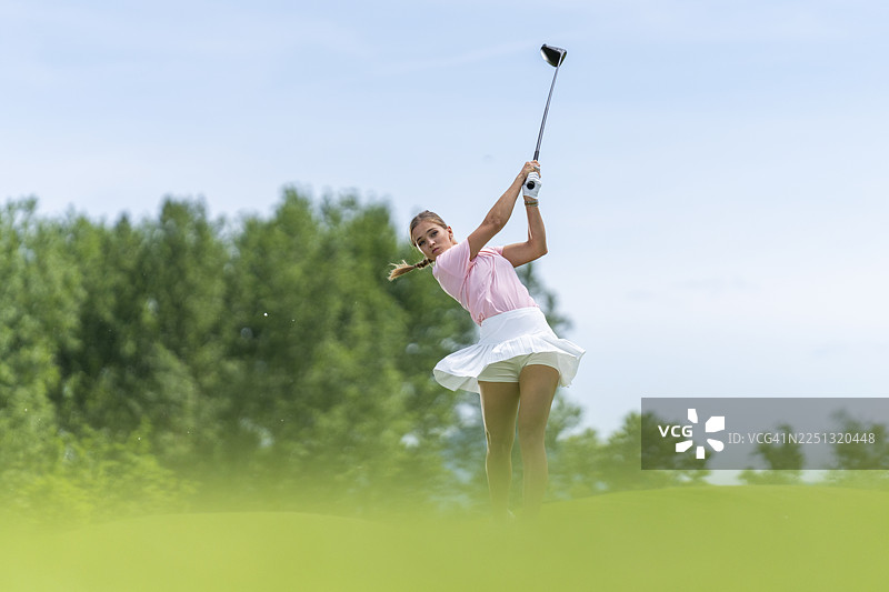 年轻的高加索女性高尔夫球手在风景优美的球场上挥动发球杆，充满喜悦图片素材