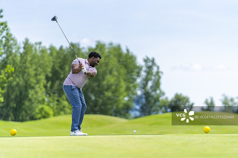 年轻的西班牙裔男性高尔夫球手在郁郁葱葱的绿色球场上专注地挥动一号木杆图片素材