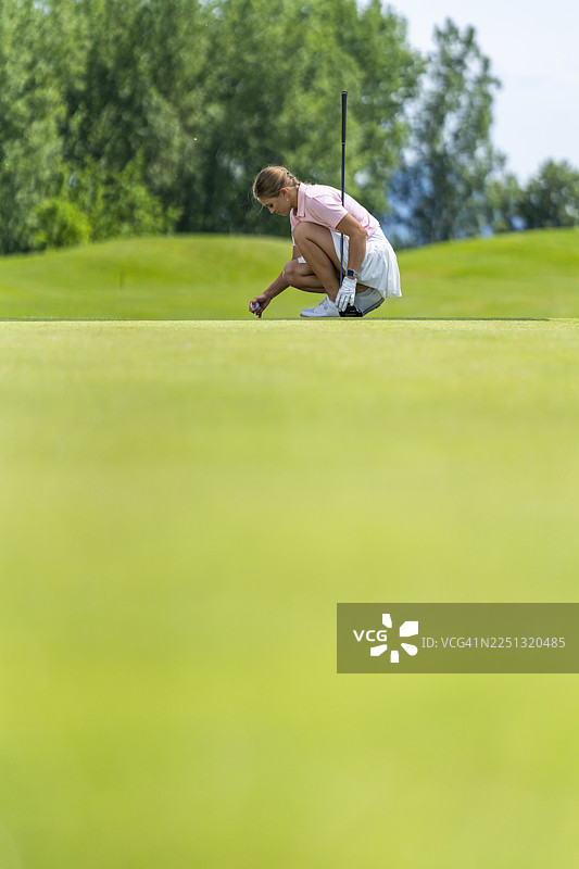 一位年轻的白人女高尔夫球手，带着专注坚定的神情，准备发球。图片素材