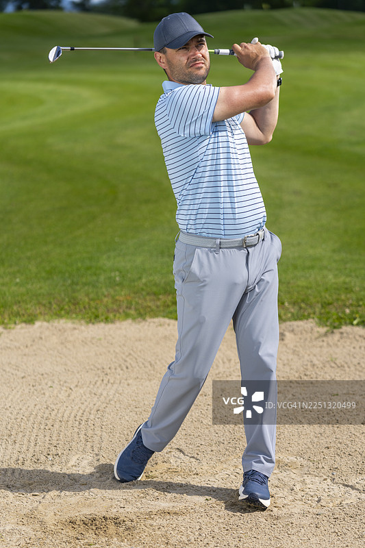 一位中年白人男性高尔夫球手，在沙坑中完成挥杆，表情专注而坚定图片素材