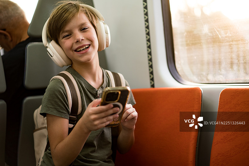 男孩戴着耳机在火车旅途中使用手机。图片素材