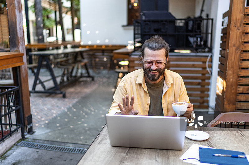 男人在咖啡馆进行视频通话时微笑着挥手图片素材