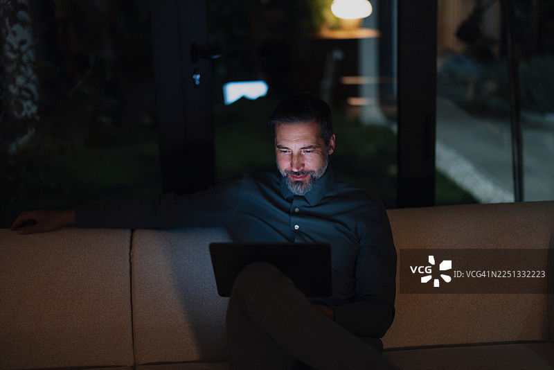 男子晚上在家里的家庭办公室沙发上用笔记本电脑工作到很晚，进行夜班工作图片素材