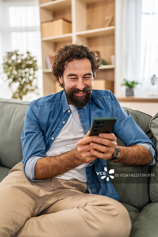 快乐的男人在家放松地躺在沙发上玩手机图片素材