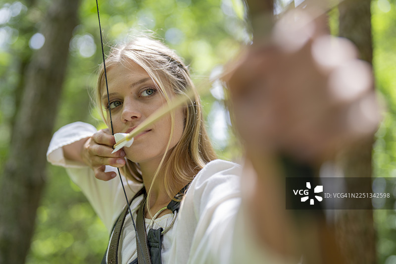 身着中世纪服饰的年轻白人女性弓箭手，专注地拉弓瞄准图片素材