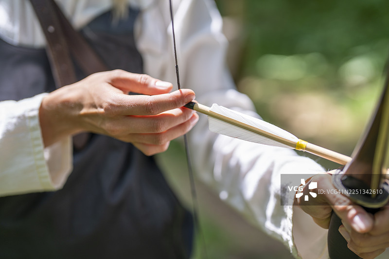 年轻的高加索女性在中世纪背景下仔细专注地准备拉弓图片素材