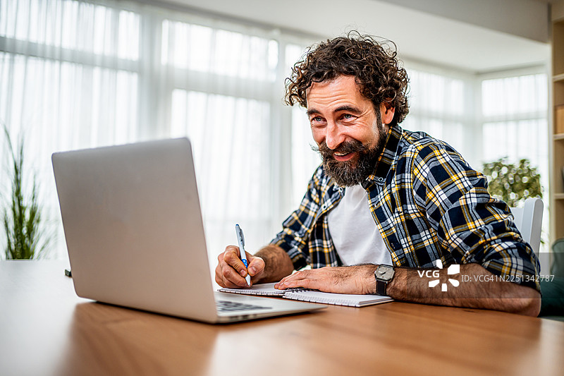 在家工作的男人，微笑着使用笔记本电脑和笔记本图片素材