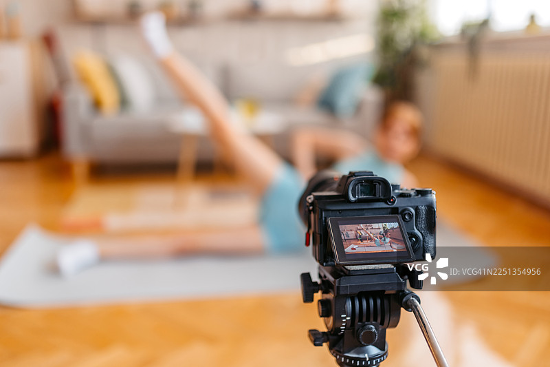 年轻女子在家拍摄教程视频，同时进行侧卧抬腿运动图片素材