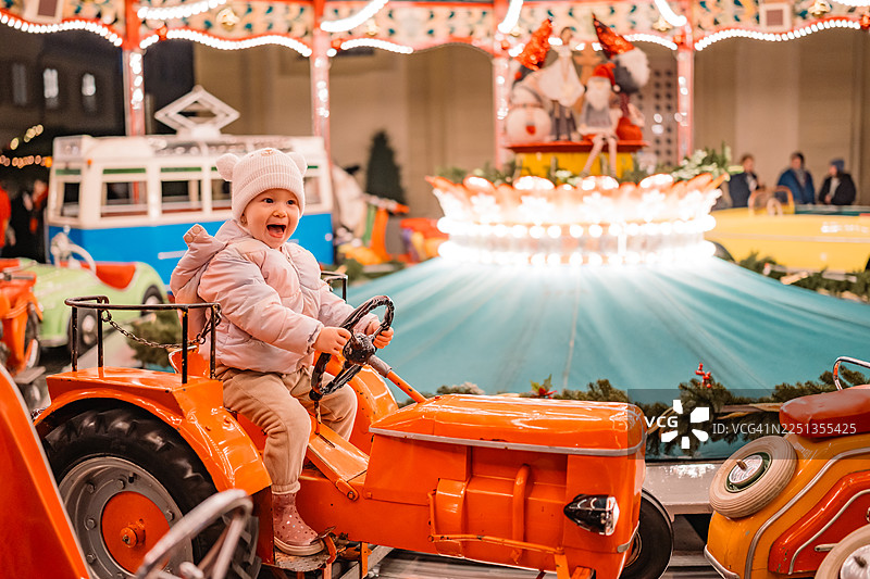 冬日节庆活动中，一名微笑的幼儿正坐在橙色拖拉机上玩耍图片素材