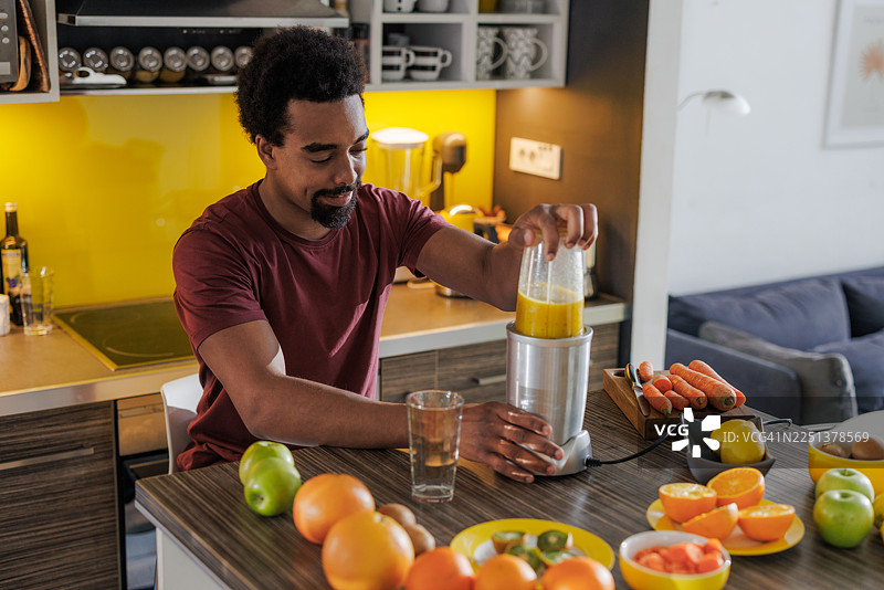 年轻男子在现代家居厨房里，用新鲜水果制作鲜榨果汁图片素材