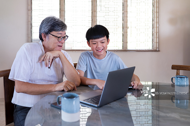 亚洲少年正在指导年迈的爷爷掌握现代电子设备图片素材