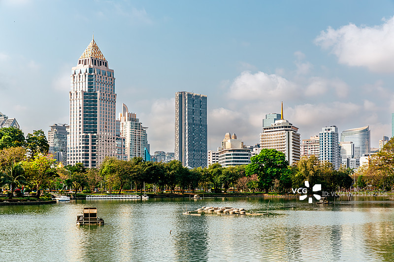 阳光明媚的日子里，从仑披尼公园望去，曼谷泰国现代摩天大楼沿着池塘排开图片素材