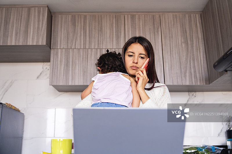 妈妈在厨房用笔记本电脑工作，孩子在旁边图片素材