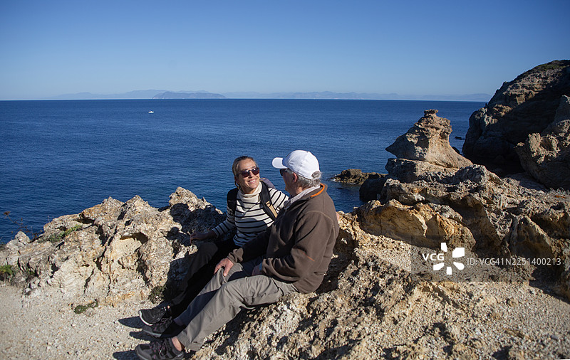 父亲和女儿在意大利蓬扎岛徒步旅行时，坐在悬崖上图片素材