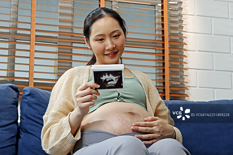 兴奋的准妈妈微笑着，温柔地拿着她的超声波照片，宣布新生命的到来图片素材