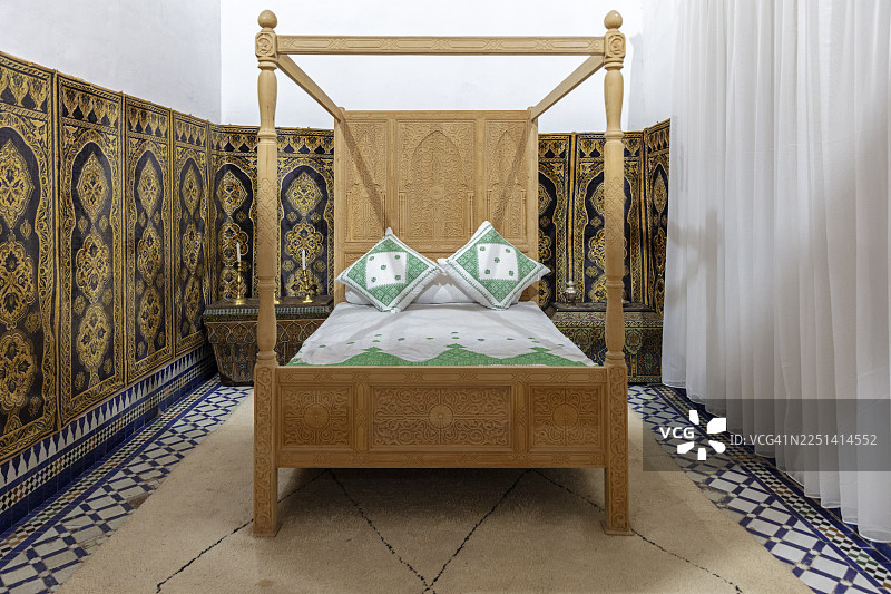 摩洛哥马拉喀什巴伊亚宫内，舒适的卧室配有传统的木制四柱床和华丽的墙壁装饰图片素材