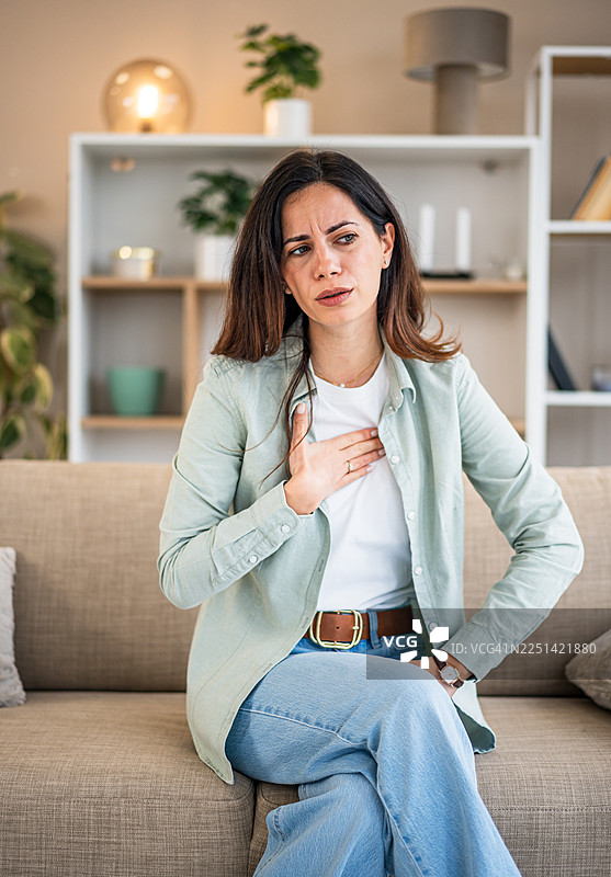 一名女子在家中坐在沙发上时感到胸痛图片素材