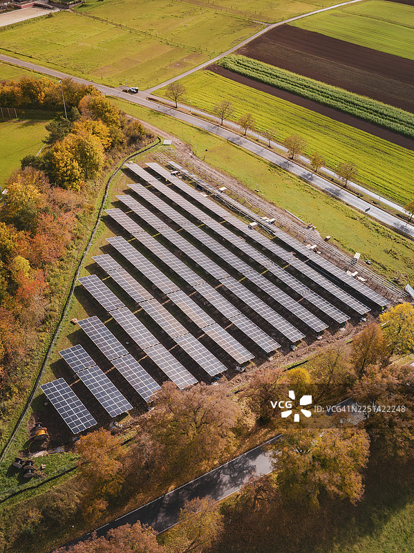 秋季背景下的太阳能发电场，周围环绕着色彩缤纷的树木和田野，鸟瞰视角，德国魏尔德施塔特（Weil der Stadt）的Bau PV Freifaechenanlage（光伏开放面积）。图片素材