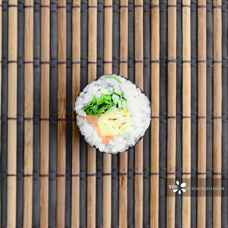 单份寿司卷，包含三文鱼、鸡蛋和生菜，放在竹帘上，俯视角度拍摄图片素材