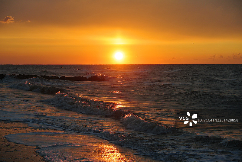 法国金色日落映照海面，温柔的海浪轻拍沙滩，构成一幅宁静而美丽的海洋风光画。图片素材