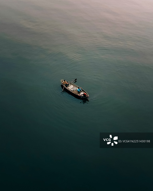 俯视视角，两人在平静的水面上驾驶着一艘小船，展现出一幅宁静而孤绝的景象图片素材