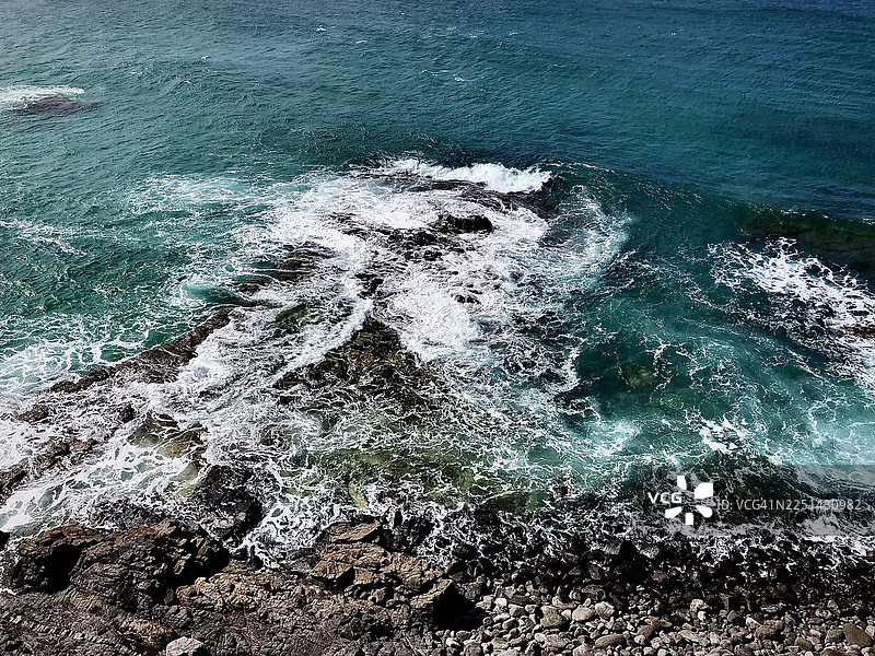 阳光明媚的日子里，高角度视角拍摄到强大的海浪拍打着崎岖的岩石，地点在西班牙拉奥利瓦。图片素材