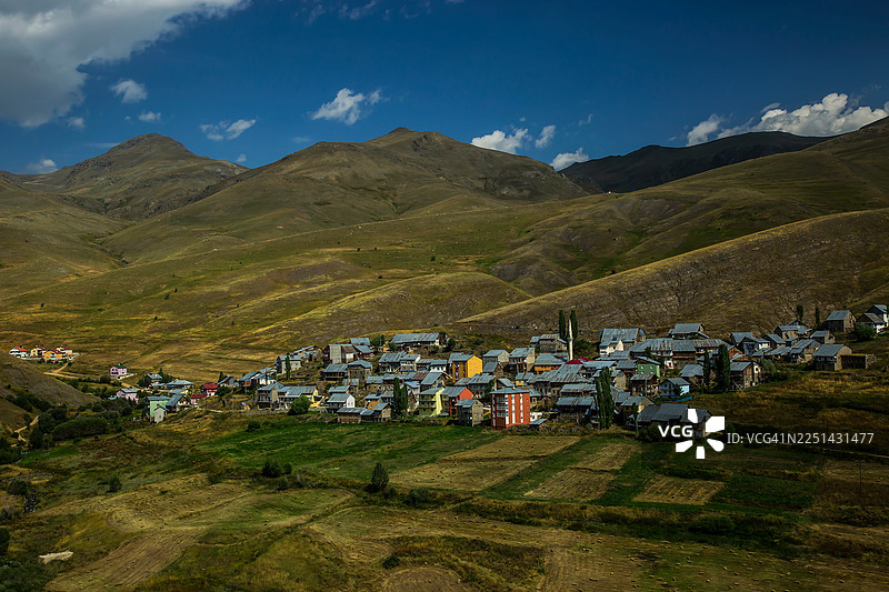 土耳其，传统村庄坐落于郁郁葱葱的绿色山谷中，天空碧蓝，点缀着几朵白云。图片素材
