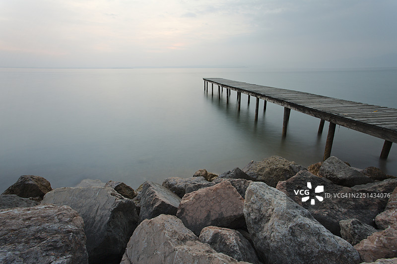 意大利巴多利诺，黄昏时分，长曝光拍摄的宁静湖泊，木制码头延伸入平静的水面，天空布满柔和的云彩图片素材
