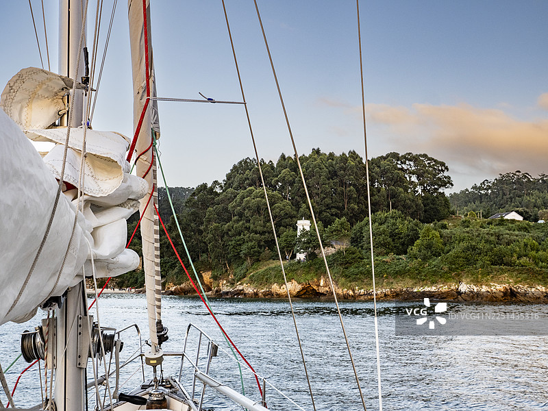 特写帆船桅杆和索具，背景是郁郁葱葱的绿色海岸线和蓝天图片素材