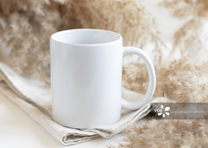 亚麻餐巾上白色咖啡杯的特写，背景是干枯的蒲苇草，营造出舒适简约的美学风格图片素材