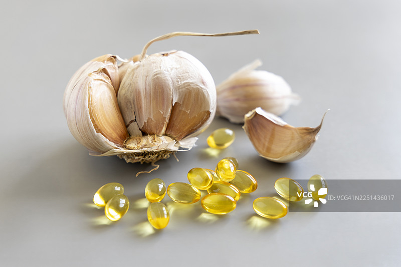 特写蒜头、蒜瓣和蒜油胶囊在灰色背景上，突出天然保健品图片素材