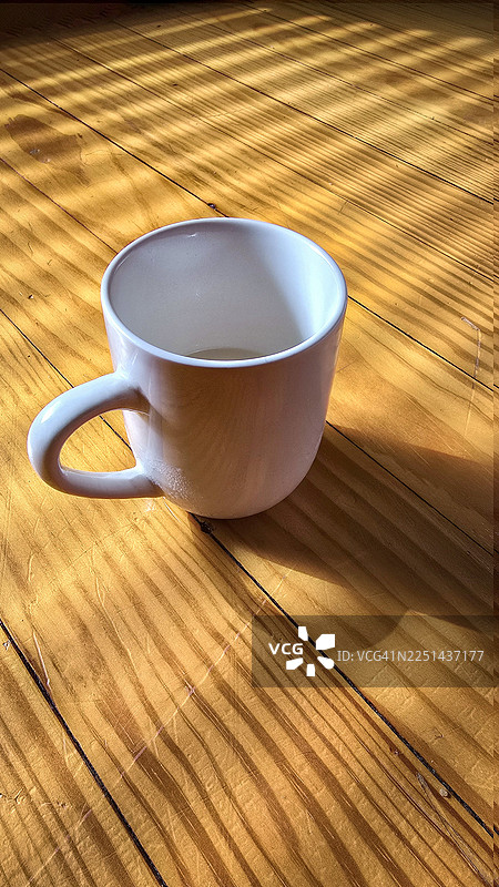 阳光条纹下的白色空咖啡杯放在木桌上，营造出舒适而富有反思的氛围图片素材