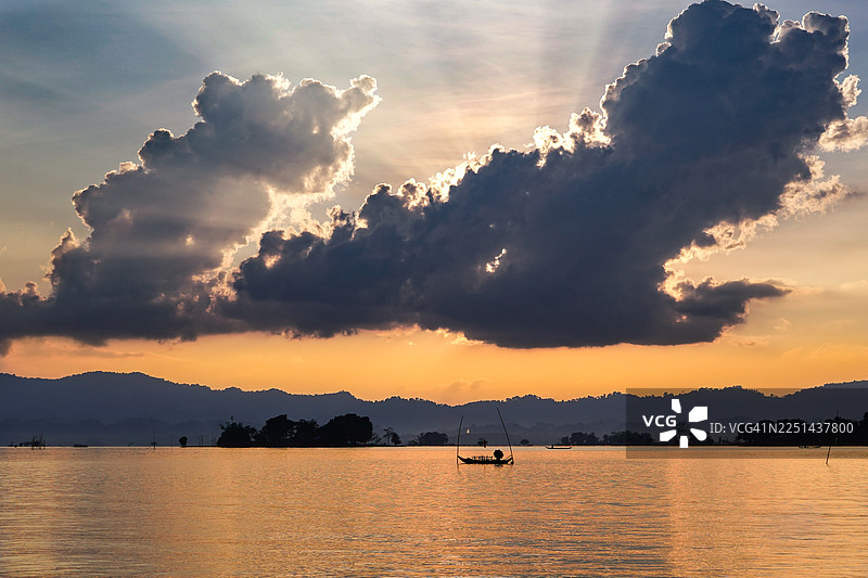 孟加拉国吉大港，绚烂的日落映衬着宁静的海面，远山和一艘小船的剪影在水上，构成一幅风景画。图片素材