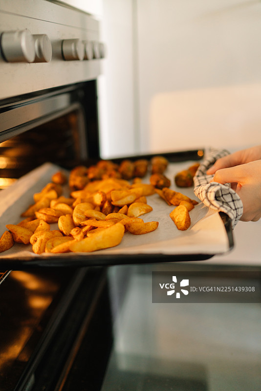 特写：一只手将装有烤土豆块的烤盘放入烤箱图片素材