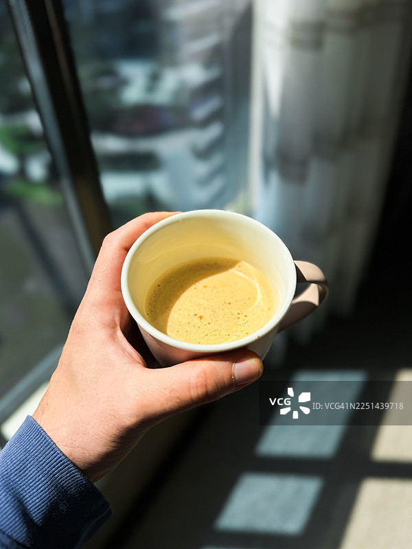 手捧着一杯咖啡，在现代环境中，光影自然。图片素材