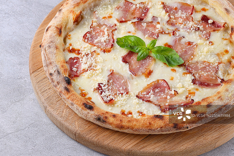 一块木质砧板上的美味披萨，上面铺着香脆培根、融化奶酪和新鲜罗勒，俯视拍摄图片素材